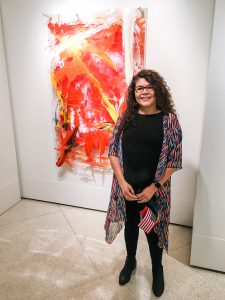 Photo of Marlenys Rojas-Reid in front of her artwork.