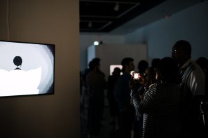 People admiring and taking pictures of one of the animation films on display at the Odyssey: Spring 2023 BFA Exhibition II.