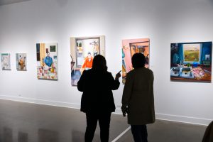 Two people admire pieces of art work hung on the wall on display at the Mimesis: Fall 2022 BFA Exhibition.