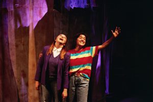 Two actors smile and embrace on stage in Irreverent