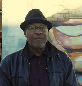 Don Harrell standing in front of the John T. Washington mural.