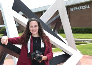 Nadia Zomorodian posing with her camera in front of the News Journal Building.